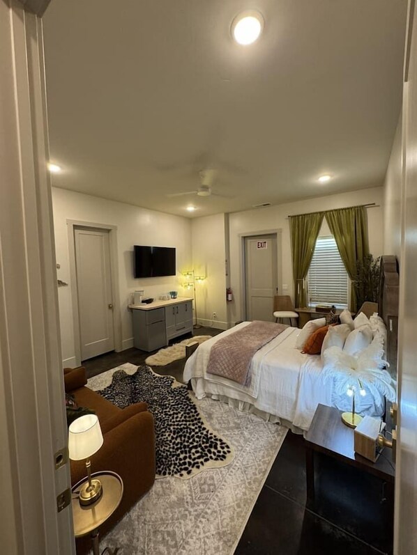 A hotel room with a bed, a desk, a chair, a television, and a door marked 'EXIT'.