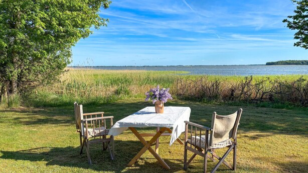 Een tafel met een bloevas, twee stoelen en uitzicht op een wateroppervlak.