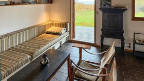 Een gezellige woonkamer met een gestreept bankje, een houten tafel en een stoel. Er is een boekenkast met boeken en een schilderij aan de muur.