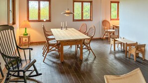 Een eetgedeelte met een houten tafel en stoelen, grote ramen en een hanglamp.