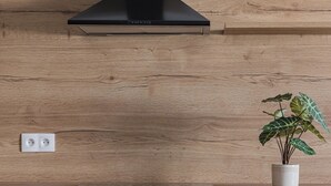 Una cocina con salpicadero de madera, una campana extractora negra, una planta blanca en maceta blanca y armarios gris oscuro con tiradores negros.