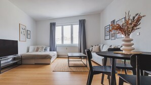 Una sala de estar moderna con un sofá, una mesa de comedor con sillas, un televisor y obras de arte en las paredes.