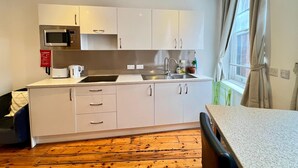 A modern kitchen with white cabinets, a microwave, a sink, and a window with curtains. - Quiet and Modern Studio 201 in Nottingham City Centre- Near Victoria (Nottingham)