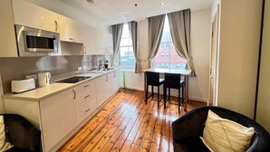 A modern kitchen with a microwave, toaster, and sink. There is a dining area with a table and chairs, and a view of buildings outside. - Quiet and Modern Studio 201 in Nottingham City Centre- Near Victoria (Nottingham)