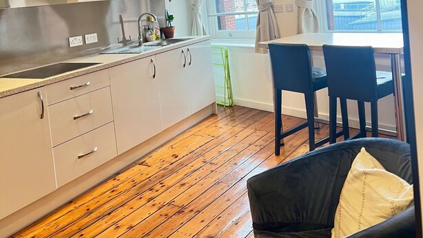 A modern kitchen with white cabinets, a wooden floor, and a dining area with a table and chairs. - Quiet and Modern Studio 201 in Nottingham City Centre- Near Victoria (Nottingham)