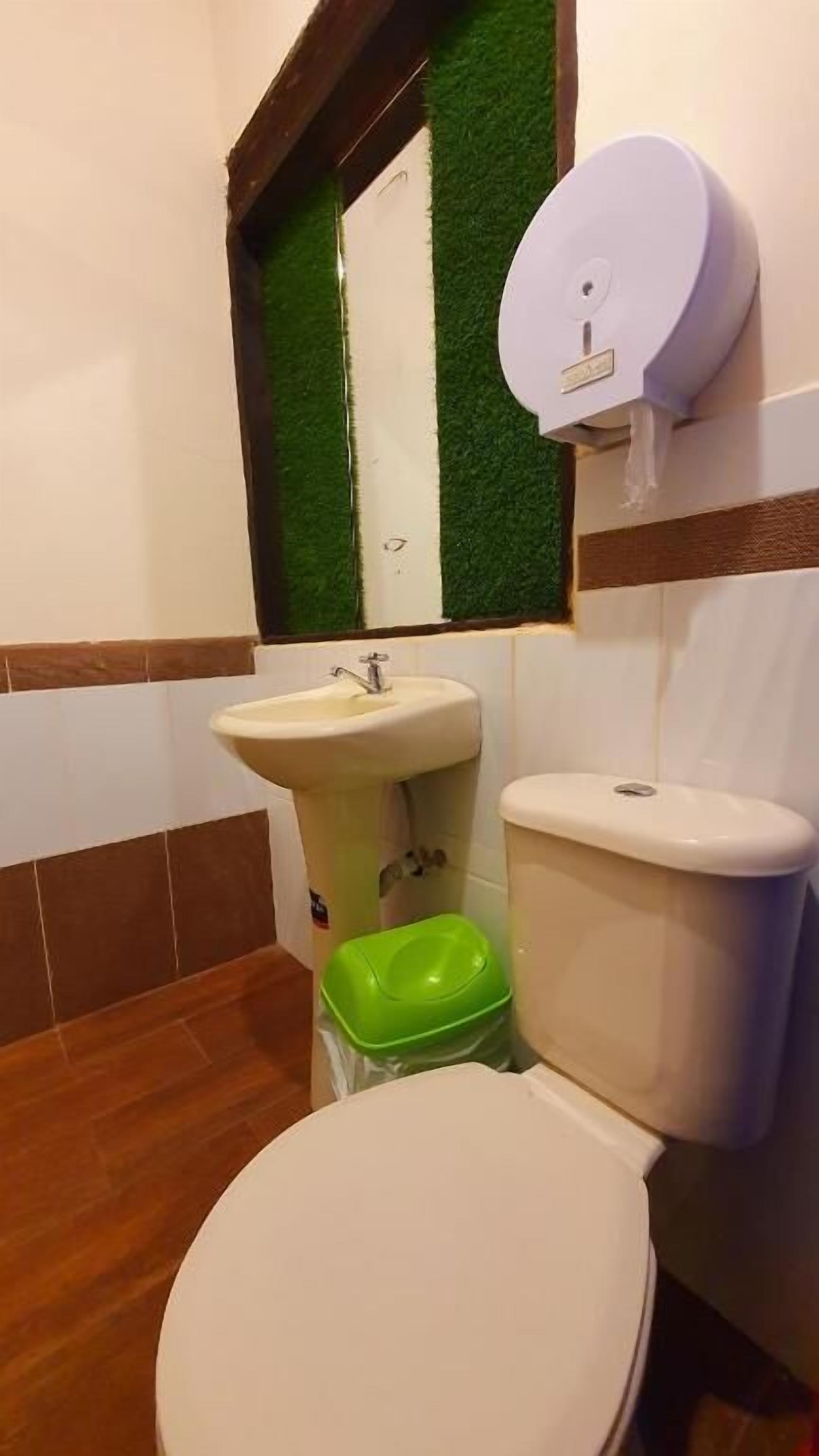 A bathroom with a toilet, sink, and green trash bin.