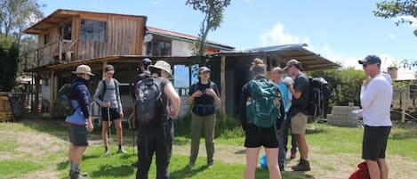 A group of people standing outdoors in front of a rustic wooden building with a sloped roof.