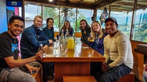 A group of people seated around a wooden table with a view of the outdoors through large windows. - Starlight Mountain Lodge (Sigchos)