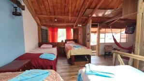 A cabin-style room with three beds, wooden floors, and a hammock. - Starlight Mountain Lodge (Sigchos)