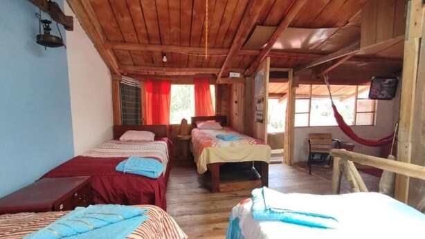 A cabin-style room with three beds, wooden floors, and a hammock. - Starlight Mountain Lodge (Sigchos)