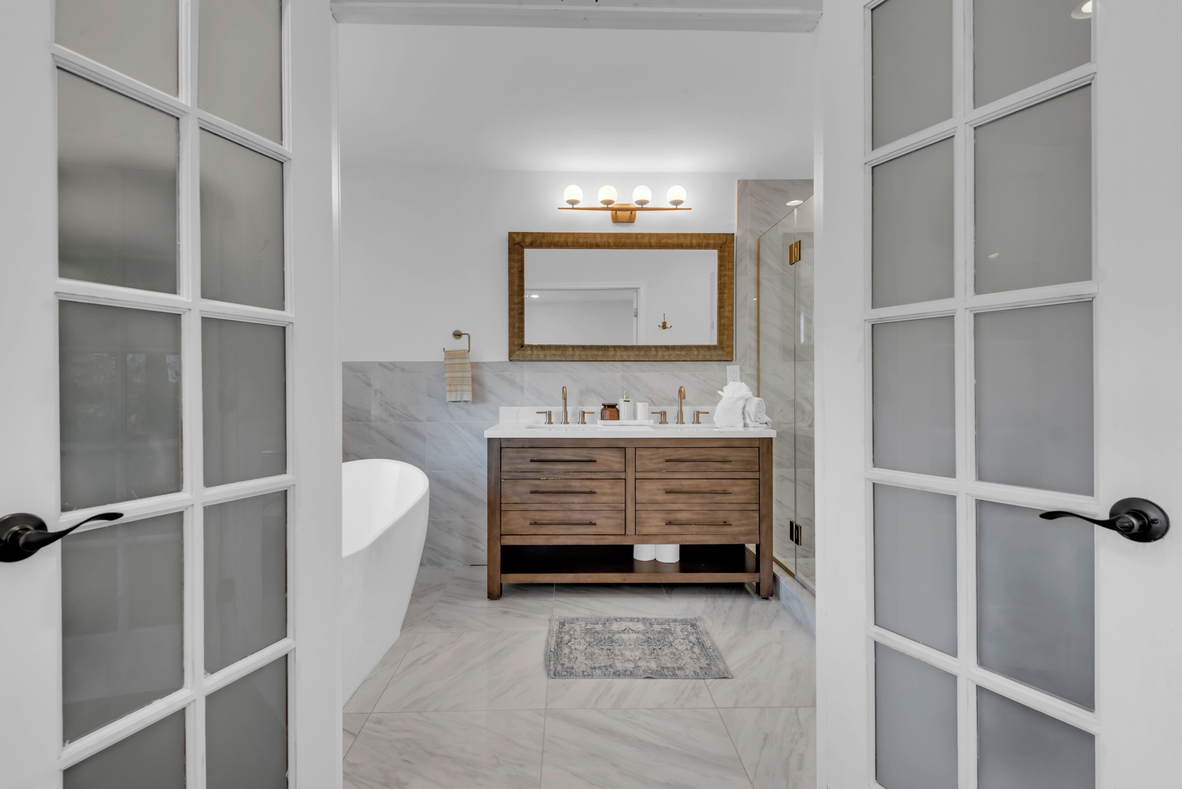 Ein Badezimmer mit einem weißen Waschbecken, einem Holzkosmetikschrank, einer Marmor-Spritzschutzwand und Milchglas-Türen.