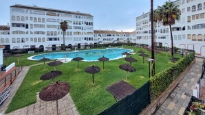 En hotelgård med swimmingpool, omgivet af hvide bygninger med buede vinduer og palmer.