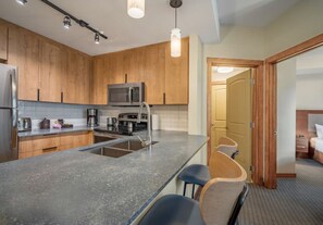 A modern kitchen with wooden cabinets, a stainless steel refrigerator, a microwave, and a large island with bar stools. - Modern condo at Falcon Crest Lodge with extra amenities (Canmore)