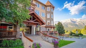 A multi-story hotel with a stone facade, a balcony, and a view of mountains. - Modern condo at Falcon Crest Lodge with extra amenities (Canmore)