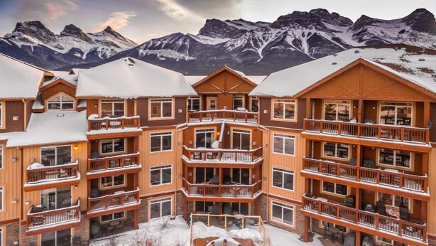 A multi-story lodge with balconies, a central courtyard, and a view of snow-covered mountains. - Modern condo at Falcon Crest Lodge with extra amenities (Canmore)
