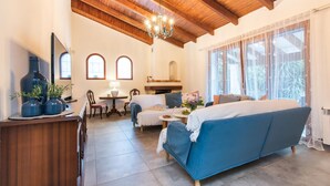 Ein gemütliches Wohnzimmer mit einem blauen Sofa, Holzbalken an der Decke, einer Chandelüstere und einem Kamin.
