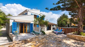 Eine Villa mit Steinterrasse, Sitzgelegenheiten im Freien und einem Swimmingpool.