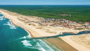 Luftaufnahme einer Küstenstadt mit Strand, einem kleinen Hafen und dichter Vegetation im Hinterland.