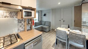 Eine kompakte Küche mit Mikrowelle, Herd und Geschirrspüler. Im angrenzenden Wohnbereich steht ein Esstisch mit Stühlen und ein Sofa.