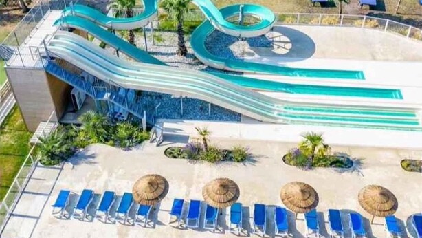 Ein Wasserpark mit mehreren Rutschen und einem Poolbereich mit Liegestühlen und Sonnenschirmen.