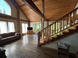 A spacious loft-style room with a wooden staircase, a large window, and a flat-screen TV. - Northwoods Retreat in Beautiful Ely, Minnesota (Ely)