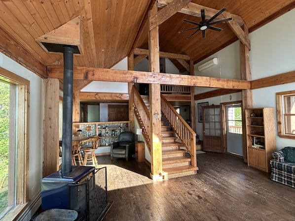 Un intérieur spacieux avec un escalier en bois, une cheminée et une vue sur l’extérieur.