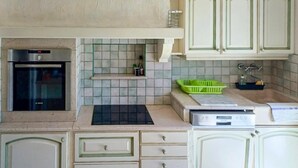 Une cuisine équipée d’un four Bosch, d’un four à micro-ondes et d’un évier. On y trouve des placards et un panier vert posé sur le plan de travail.