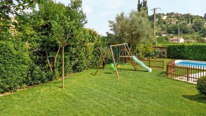Un jardin avec une balançoire, un toboggan, une piscine clôturée et une pelouse bien entretenue.