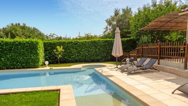 Une piscine avec une terrasse carrelée, un petit jardin et une clôture en bois.