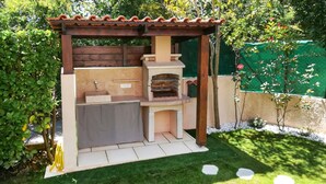 Une pergola en bois dotée d’un four à pizza intégré et d’un évier, le tout entouré d’une pelouse bien entretenue.