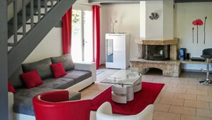 Un salon moderne avec un canapé gris, des coussins rouges, une table basse en verre et une cheminée en pierre.