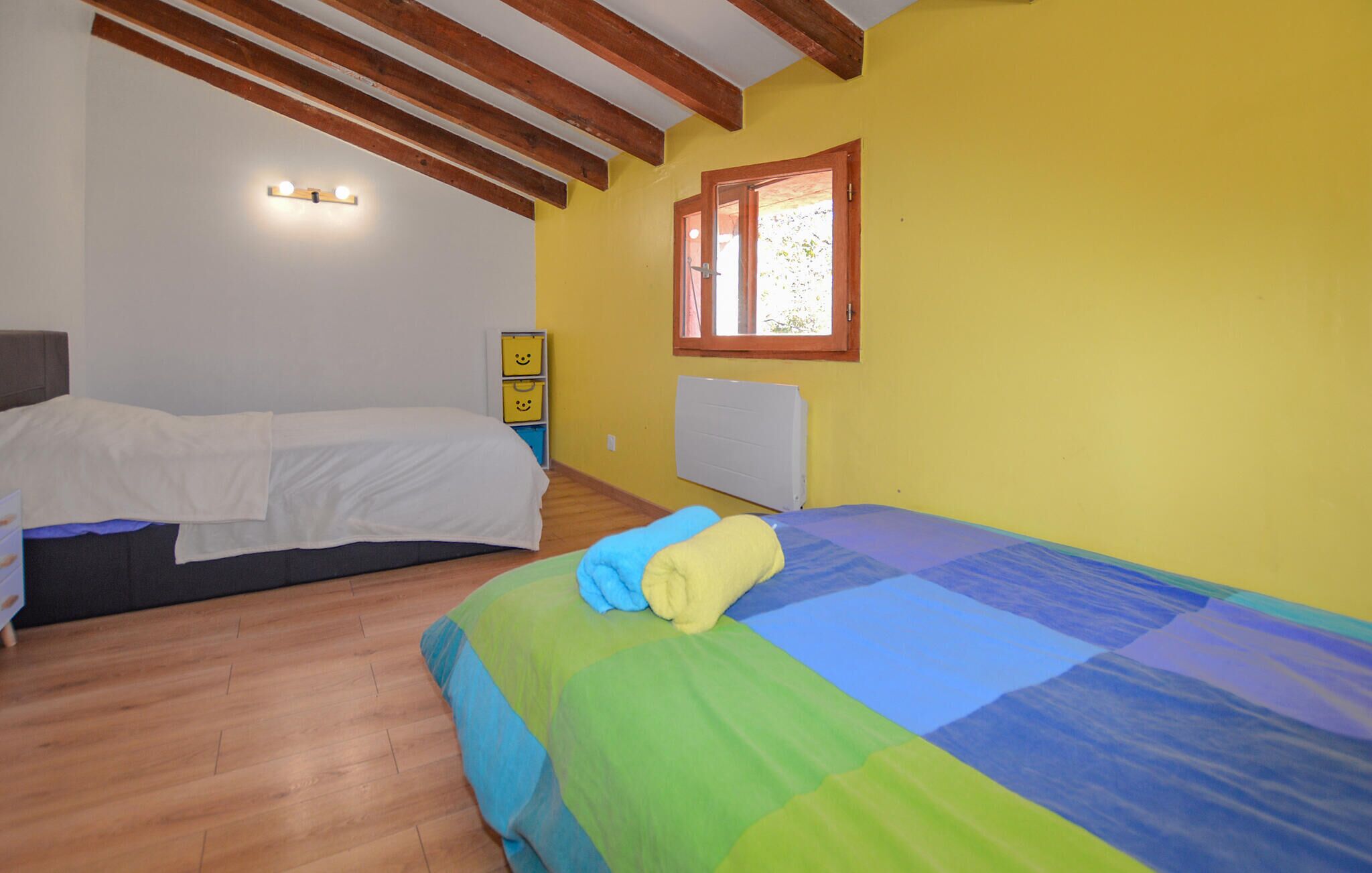 A room with two beds, wooden beams on the ceiling, a window with a view, and a radiator on the wall.