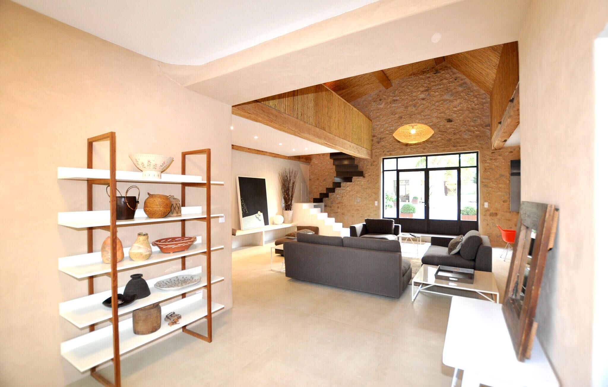 A spacious living area with a high ceiling, a staircase, and a large window providing natural light.