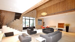 Een ruime woonkamer met een hoge plafond, stenen muren en een trap naar een hoger gelegen verdieping.