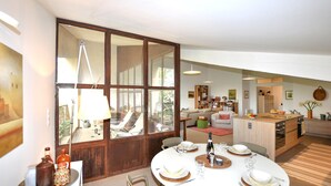 Un espace repas moderne avec une grande fenêtre, une table à manger dressée pour quatre personnes et une cuisine en arrière-plan.