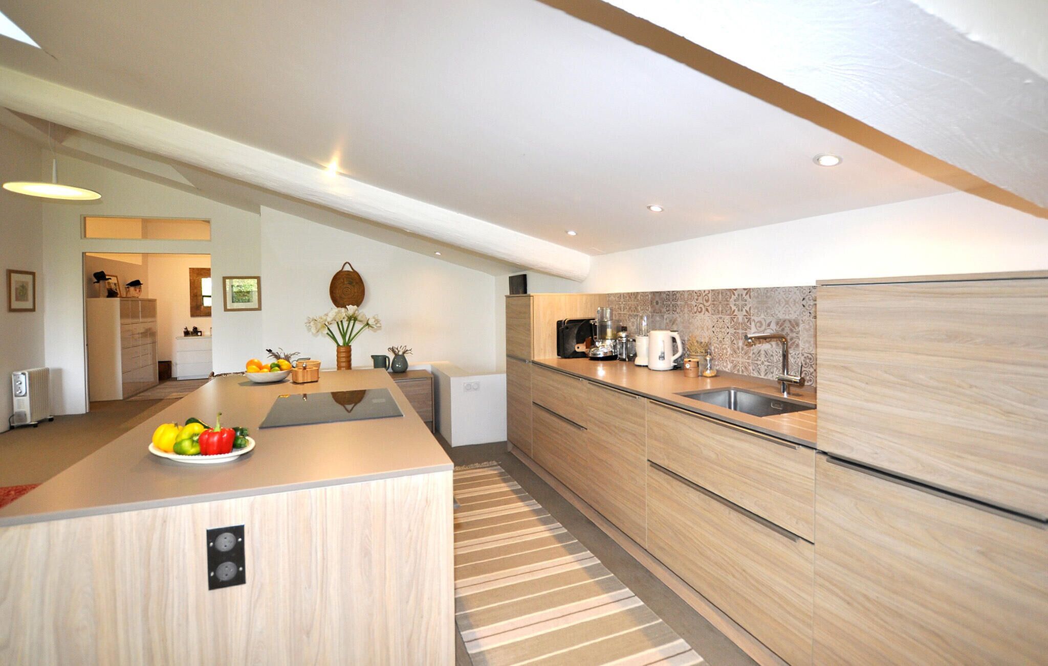Una cocina moderna con armarios de madera, una isla central con fruta, horno empotrado y un amplio ventanal.