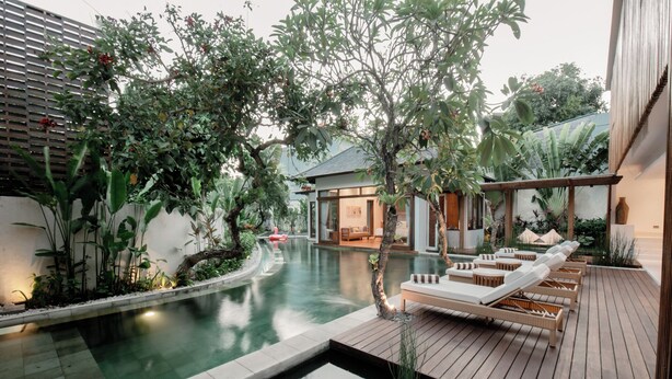 A modern outdoor pool area with a wooden deck, lounge chairs, and a small waterfall feature. - Villa Seminyak 4BR w/pool close to Petitenget (Badung Regency)