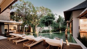 A poolside area with lounge chairs, a wooden deck, and a view of a modern building with a balcony. - Villa Seminyak 4BR w/pool close to Petitenget (Badung Regency)