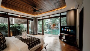 A modern hotel room with a large bed, a television, and a view of an outdoor swimming pool. - Villa Seminyak 4BR w/pool close to Petitenget (Badung Regency)