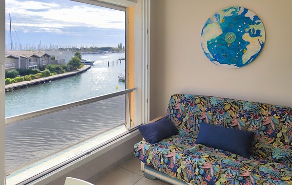 A room with a view of a river, a colorful sofa with two cushions, and a round wall decoration. - Cozy apartment in Agde with house sea view (Agde)