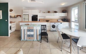 A modern kitchen with a central island, a washing machine, and a dining area with chairs. - Cozy apartment in Agde with house sea view (Agde)