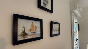 Three framed artworks on a wall, a window with decorative elements, and a white lamp.