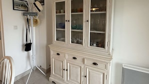 A room with a white cabinet containing glassware and dishes, a hat rack, and framed pictures on the wall.