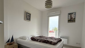 A bedroom with a bed, a small wooden nightstand, a window with a view of the outside, and a ceiling light fixture.