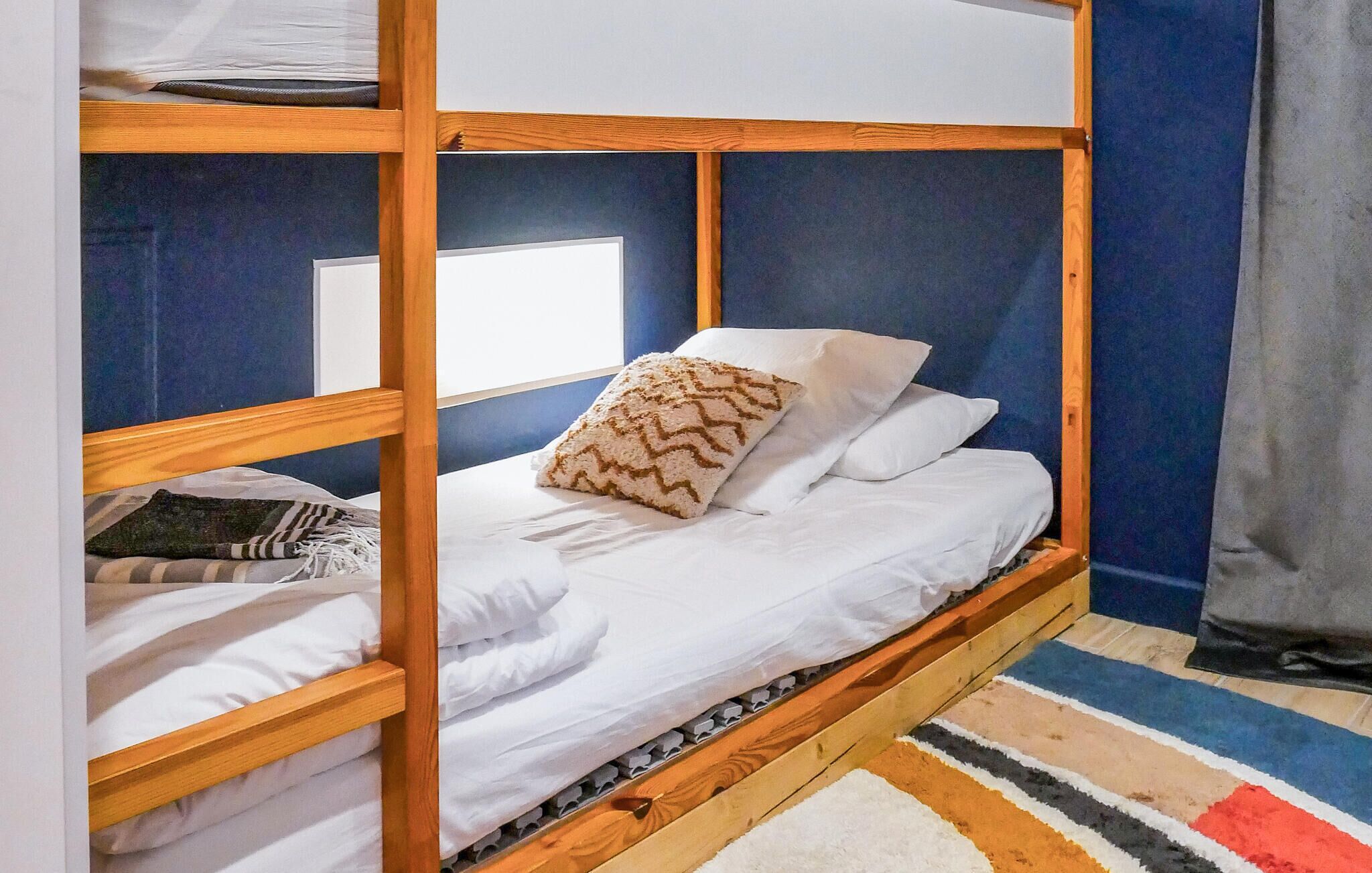 A bunk bed with white bedding and a patterned pillow, set against a blue wall with a window.