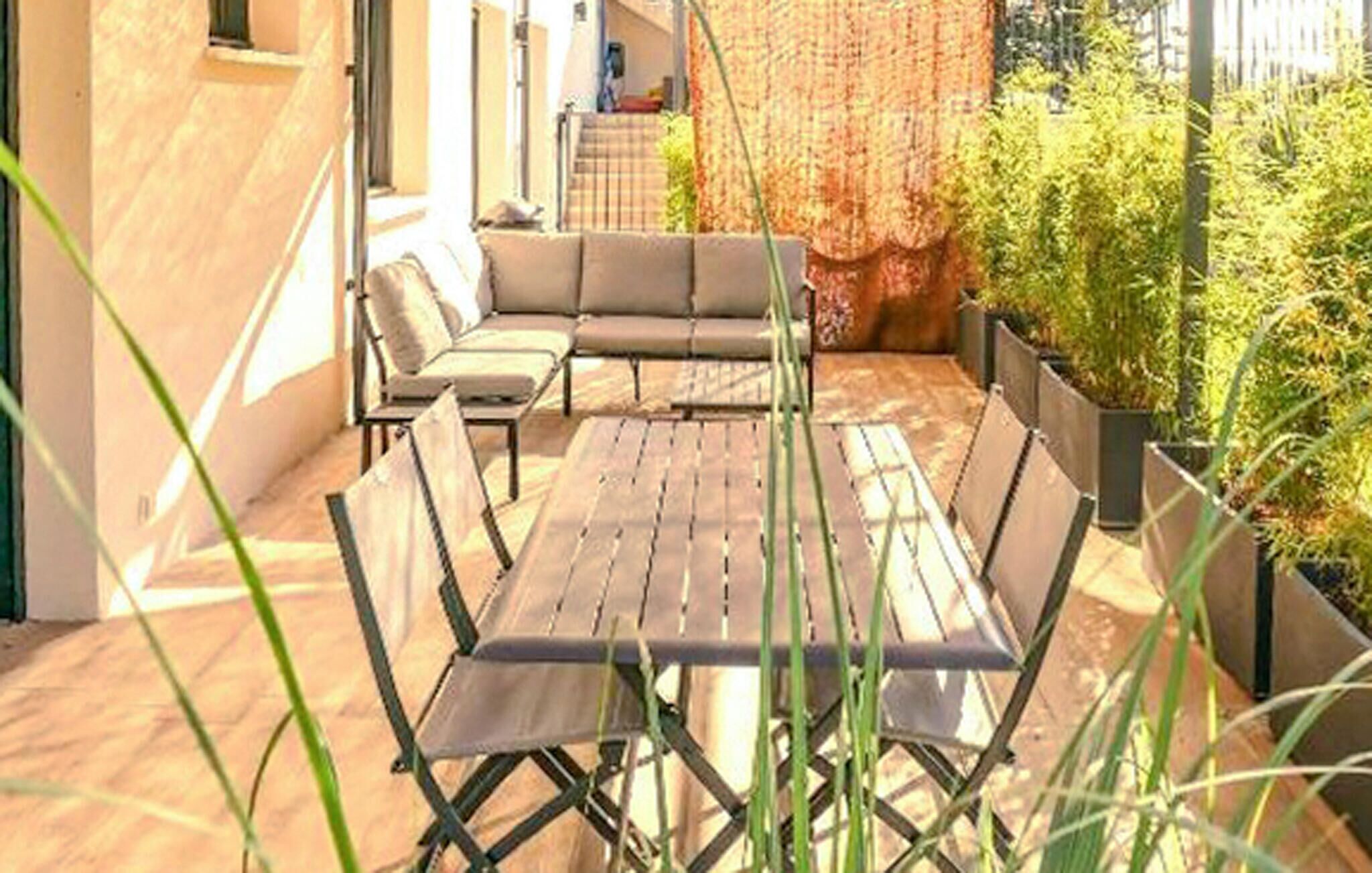 An outdoor seating area with a wooden table and chairs, surrounded by potted plants and a brick wall.