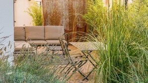 A modern outdoor seating area with a sofa and a table, surrounded by lush greenery and a decorative fence. - 2 bedroom cozy home in Allan (Allan)
