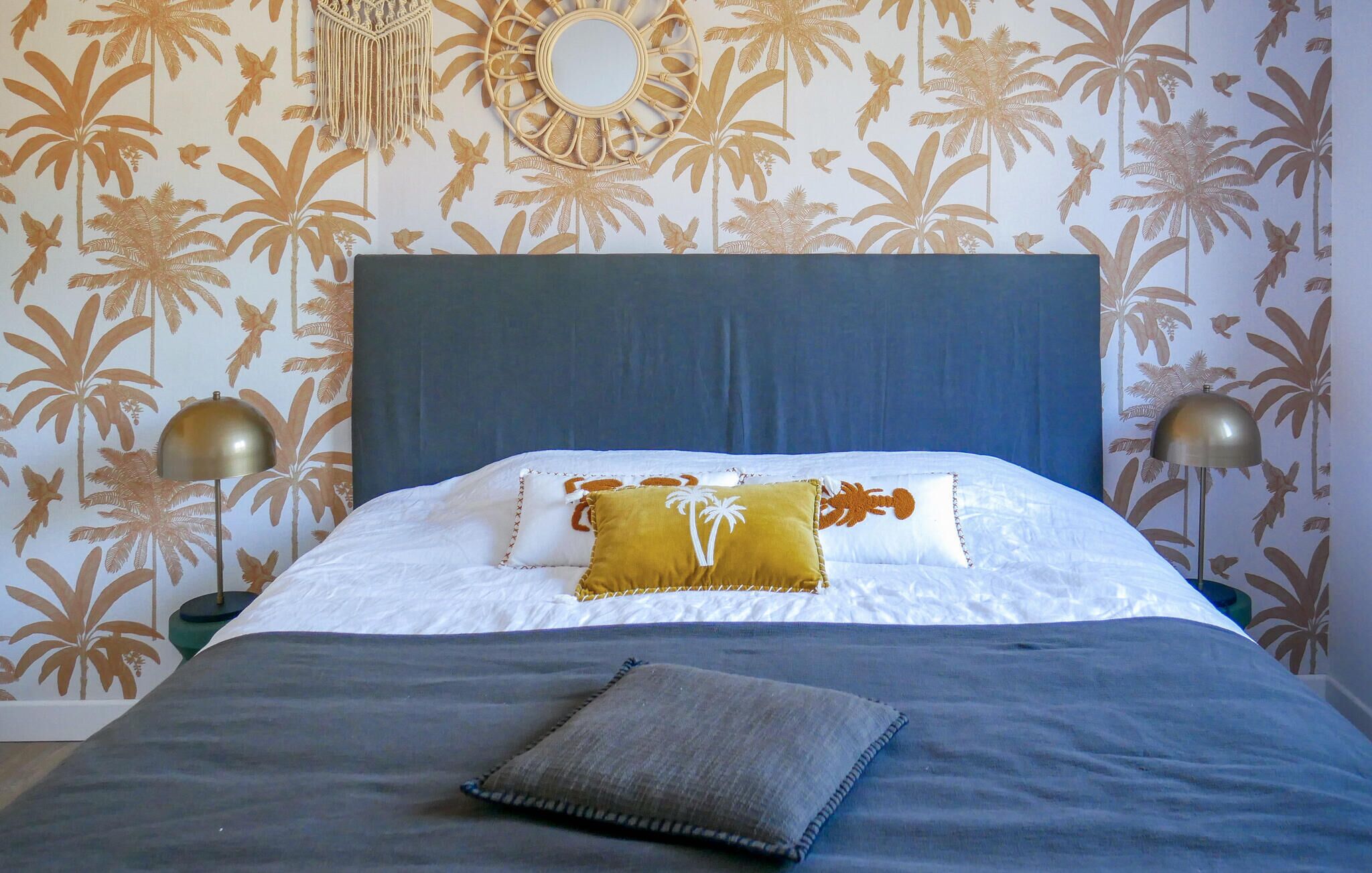 A neatly made bed with a blue headboard, two bedside lamps, and a decorative wall hanging.