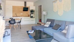A modern living room with a grey sofa, a glass coffee table, and a dining area with a wooden table and chairs. - 2 bedroom cozy home in Allan (Allan)