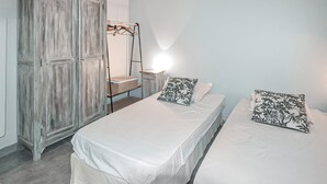 Camera da letto con due letti, un armadio, uno specchio e un tavolino con un cesto.